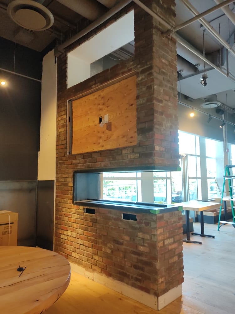 Brick chimney feature mid-construction with TV opening — Tap & Barrel